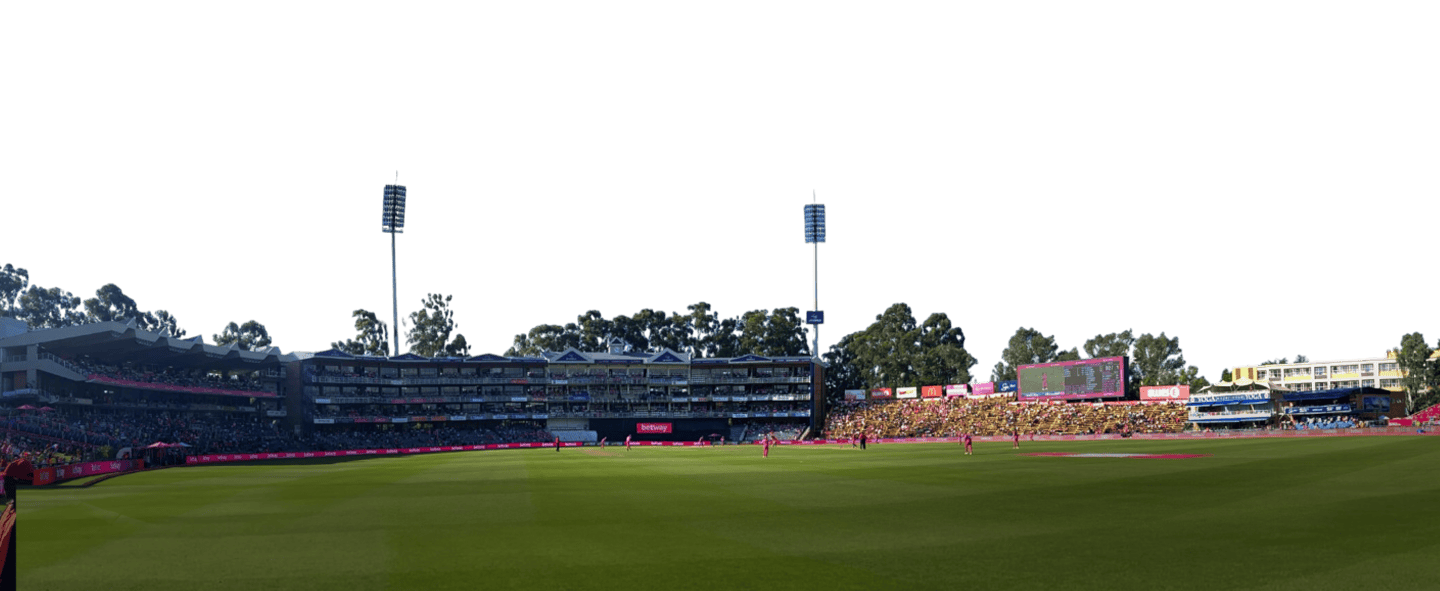 Wide view of a cricket stadium during a match, with players on the pitch and stands full of spectators